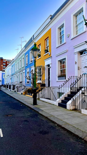 A paved sidewalk running alongside a row of elegant white terraced houses with black wrought iron fences. The fence is partially obstructed by a blue bicycle locked to it, with a front basket visible.